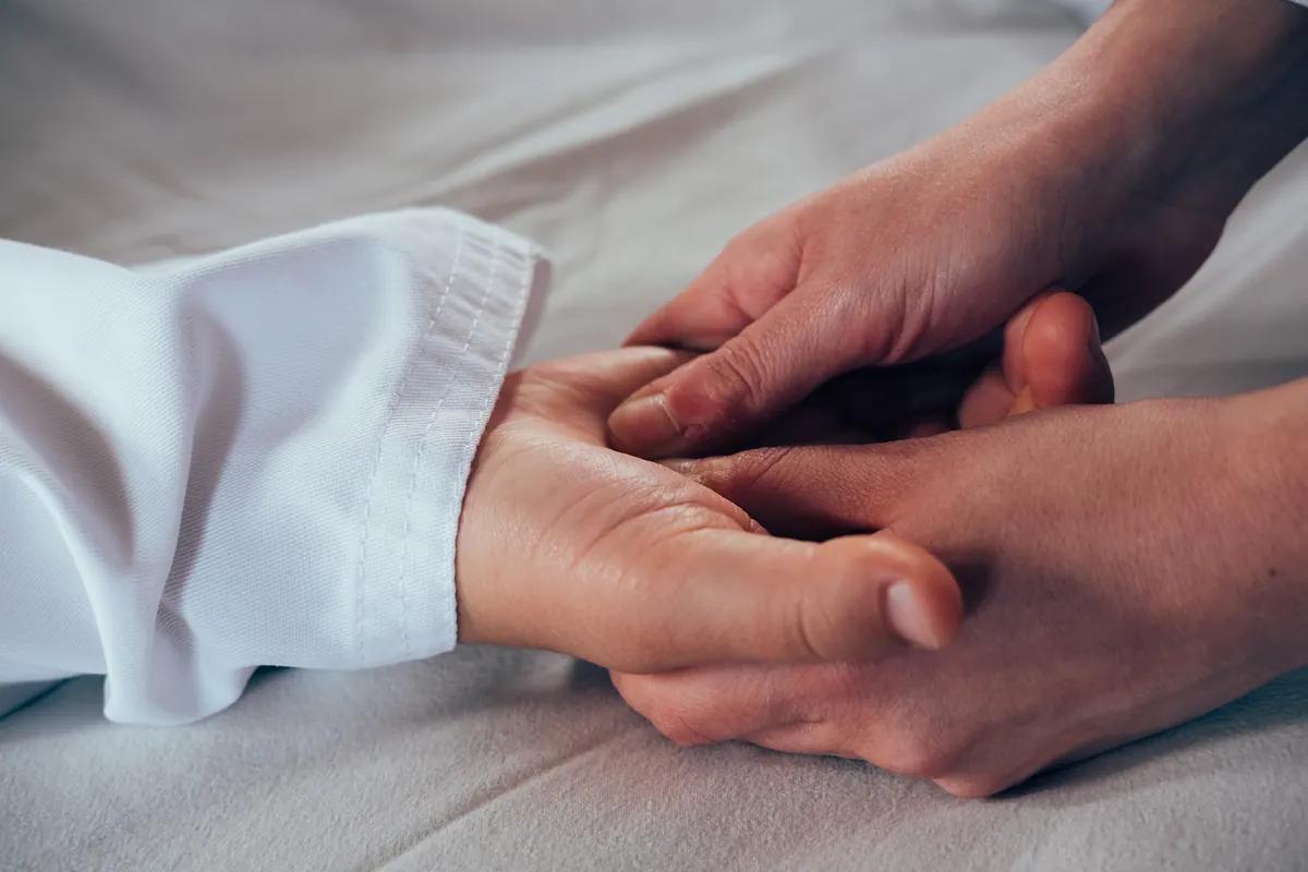 Primo piano: le mani di Cecilia accolgono la mano di una persona distesa, il polso che esce dalla manica del kimono.